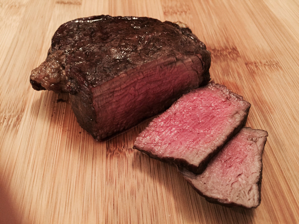 Photo of cooked rare fillet mignon partially sliced on a cutting board
