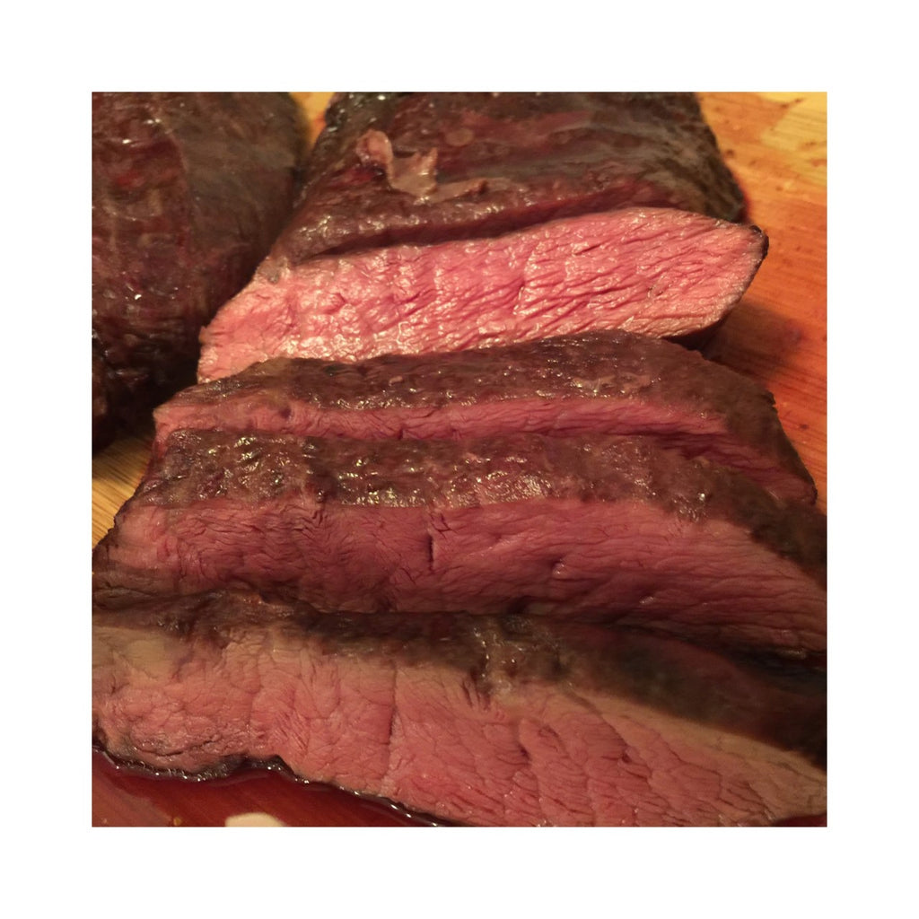 Photo of cooked sliced rare flat iron steak on a wood cutting board