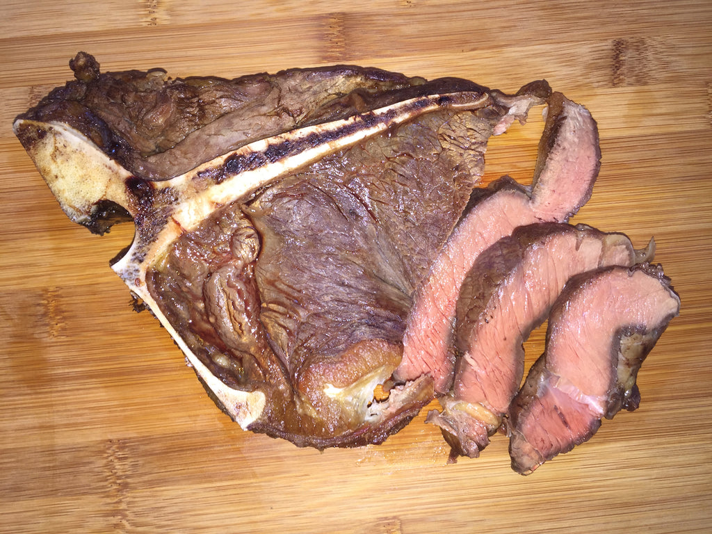 Photo of a cooked t-bone steak with 3 slices on a wood board