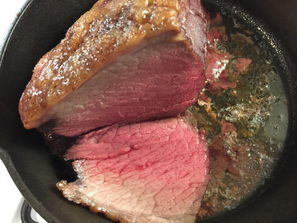 Photo of cooked rare sirloin tip roast with one slice in a cast iron pan