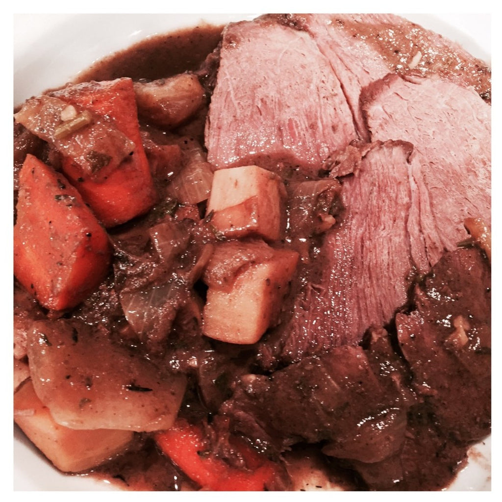 Picture of cooked sliced chuck roast on a white plate with potatoes, carrots and gravy