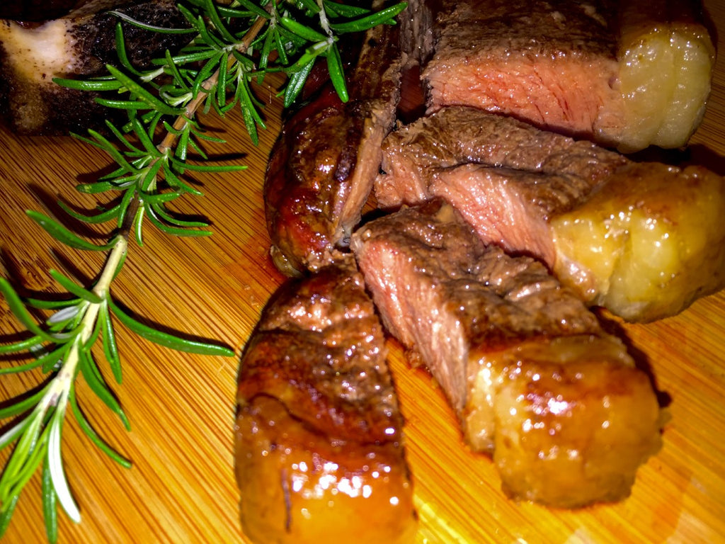 Photo of sliced cooked new york steak on a cutting board with a sprig of rosemary
