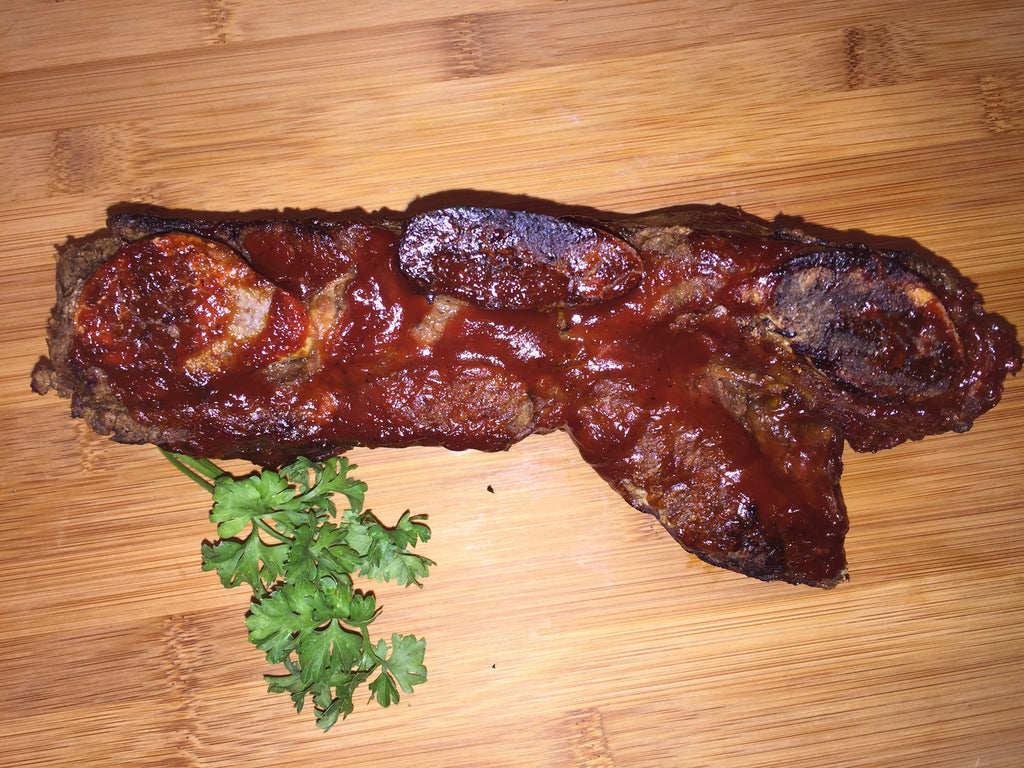 Photo of cooked short ribs covered with barbeques sauce on a wood cutting board with a sprig of parsley