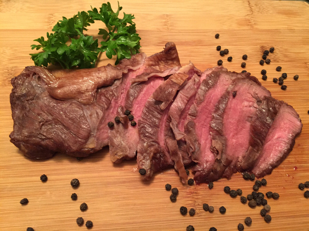Photo of rare cooked sliced skirt steak on a wood cutting board surrounded by pepper corns and a sprig of parsley